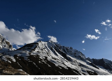 Dramatic snow-covered mountain peaks featuring a rugged landscape of ice, sand, and sharp rocky formations in the high-altitude Himalayas. The contrast between white snowy summits, barren sandy slopes, and jagged rocks creates a breathtaking and raw alpine scenery. Ideal for themes of adventure, nature, geology, travel, and remote mountain landscapes.