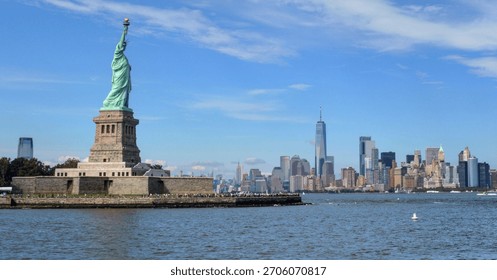 Dramatic soft-blue sky over the New York City skyline with the Statue of Liberty visible in the foreground. A clear and vibrant view of Manhattan’s waterfront with atmospheric clouds and calm light.