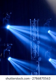 Dramatic stage light shining bright blue beam through thick fog from metal truss structure creating energetic concert atmosphere with professional spotlight equipment