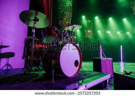 A dramatic stage view featuring a vibrant drum kit under green and purple lights, with a guitar and amp in the background, creating a dynamic musical performance atmosphere