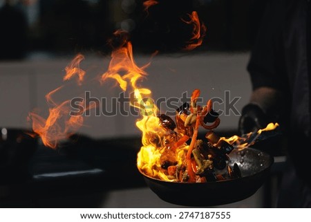 Dramatic stir fry flames in kitchen with vegetables on fire, man chef prepares food.