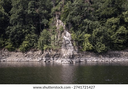 Dramatic stone cliff face rising vertically from the water surface at the edge of Dalesice reservoir