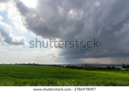 Dramatic storm cloud and downpour rain over green grass field. Scenic mediterranean countryside landscape with dark weather atmosphere and distant salt lake under overcast sky. Cyprus.