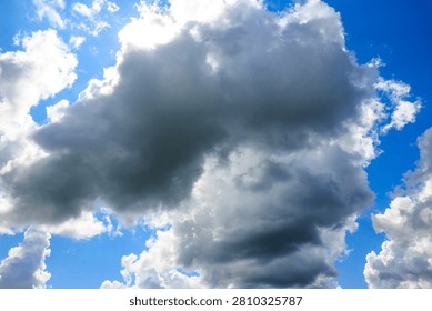 Dramatic storm clouds drifting across a brilliant blue sky, bright sun rays peeking through massive fluffy cumulus formations creating an intense atmospheric contrast on a clear summer day