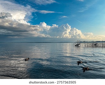 Dramatic storm clouds forming above calm Lake Balaton with quiet water reflections and lonely pier in Hungary
Epic cumulonimbus cloudscape over peaceful lake surface with metal pier silhouette at Balaton shoreline
Massive summer thundercloud formation above tranquil water landscape at Lake Balaton Hungary
Moody sky and towering clouds above calm lake h