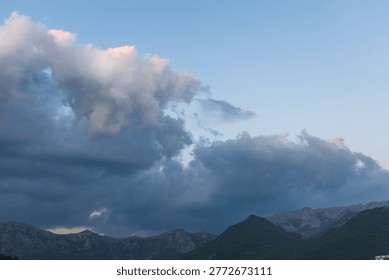 Dramatic storm clouds gather above a rugged mountain range at dusk, casting deep blue shadows while soft pink light edges the clouds for a moody, atmospheric natural landscape and weather scene.