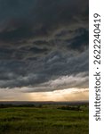 Dramatic storm clouds gather over the green prairies of Washington County, Oklahoma, as golden light breaks through the horizon during a powerful summer thunderstorm.