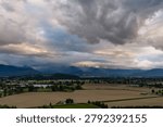Dramatic storm clouds gather over Chilliwack farmland and distant mountains in the Fraser Valley, BC, Canada.