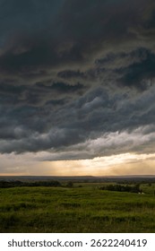 Dramatic storm clouds gather over the green prairies of Washington County, Oklahoma, as golden light breaks through the horizon during a powerful summer thunderstorm.