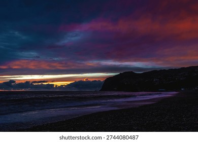 Dramatic storm clouds gather over the rugged volcanic shoreline of Madeira as Atlantic waves crash onto a dark pebble beach at dusk.



