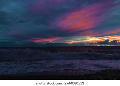 Dramatic storm clouds gather over the rugged volcanic shoreline of Madeira as Atlantic waves crash onto a dark pebble beach at dusk.



