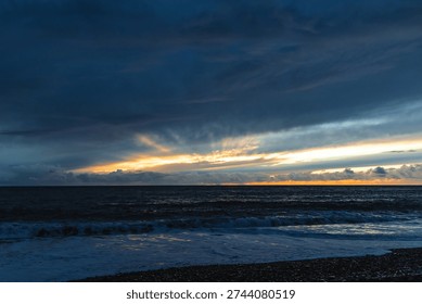 Dramatic storm clouds gather over the rugged volcanic shoreline of Madeira as Atlantic waves crash onto a dark pebble beach at dusk.



