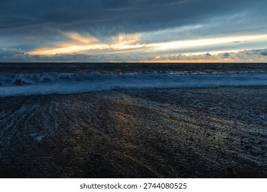 Dramatic storm clouds gather over the rugged volcanic shoreline of Madeira as Atlantic waves crash onto a dark pebble beach at dusk.



