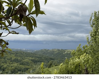 Dramatic storm clouds gather over lush forested hills and vineyards in the Italian countryside