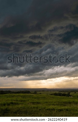 Dramatic storm clouds gather over the green prairies of Washington County, Oklahoma, as golden light breaks through the horizon during a powerful summer thunderstorm.