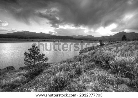 Dramatic storm clouds gather over a mountain lake and rolling landscape rendered in monochrome.