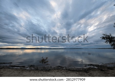Dramatic storm clouds gather over a mountain lake and rolling landscape rendered in monochrome.