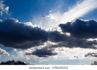 Dramatic storm clouds gathered in the bright blue sky with brilliant rays of sunlight breaking through the dark formations creating a moody and picturesque contrast over the horizon