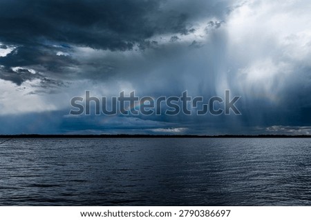 Dramatic storm clouds with heavy rain over lake water before thunderstorm