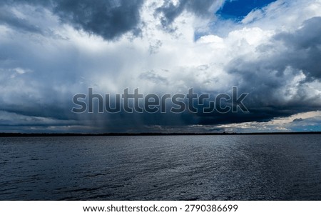 Dramatic storm clouds with heavy rain over lake water before thunderstorm