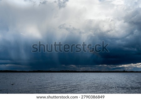 Dramatic storm clouds with heavy rain over lake water before thunderstorm