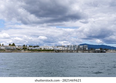 Dramatic storm clouds hover over a waterfront pier and seaside homes in Sidney on Vancouver Island, BC, Canada, conveying moody coastal atmosphere.