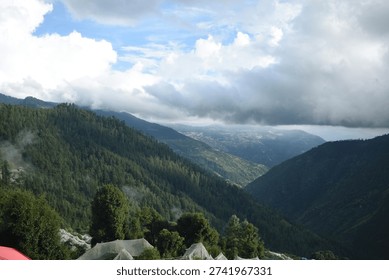Dramatic storm clouds hovering over a lush green Himalayan mountain valley in Himachal Pradesh, India. Scenic landscape featuring layered hills, dense forest, and misty mountain ridges under an overcast sky. Moody atmosphere and natural beauty create a powerful nature background ideal for travel, environment, and outdoor themes.