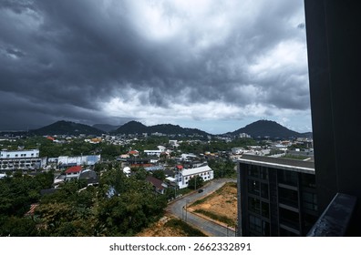 Dramatic storm clouds loom over a city surrounded by green hills, creating a captivating and contrasting atmosphere between urban construction and natural beauty