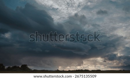 Dramatic storm clouds loom over flat rural landscape. Dark and heavy clouds create an ominous and intense atmosphere during daytime.