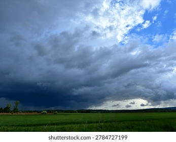 Dramatic storm clouds over a green agricultural field, impending rain weather landscape.
