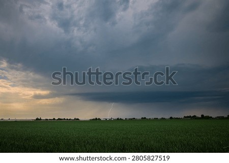 Dramatic storm clouds over green farmland field with lightning bolt and rain shaft