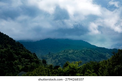 Dramatic storm clouds over lush green mountain forest wilderness. A moody landscape showing a dense green mountain range under overcast sky A symbol of nature's power and pristine wilderness.