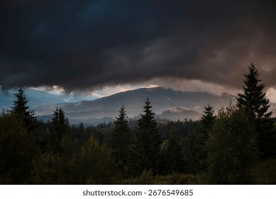 Dramatic storm clouds over a misty forest landscape with mountains.