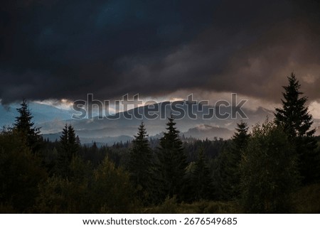 Dramatic storm clouds over a misty forest landscape with mountains.