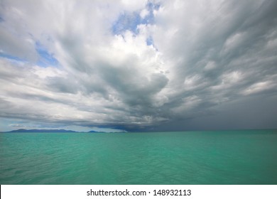 dramatic storm clouds over tropical island and blue-green sea amidst sunny blue skies