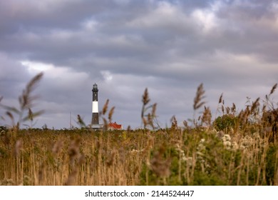 Dramatic Storm Clouds Overhead A Tall Stone Lighthouse With Beach Grass In The Foreground. Fire Island, Long Island New York