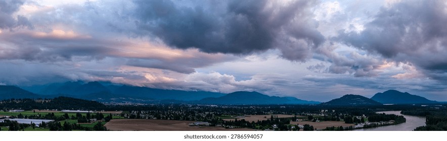 Dramatic storm clouds roll over the agricultural valley, river and mountains near Chilliwack, British Columbia, Canada at sunset.