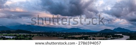 Dramatic storm clouds roll over the agricultural valley, river and mountains near Chilliwack, British Columbia, Canada at sunset.