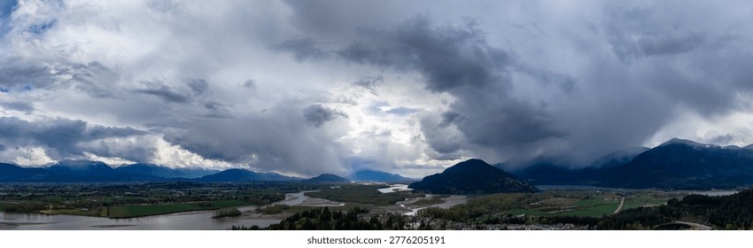 Dramatic storm clouds rolling over the Fraser Valley river floodplain and mountains; Cloudscape in Fraser Valley, British Columbia, Canada.