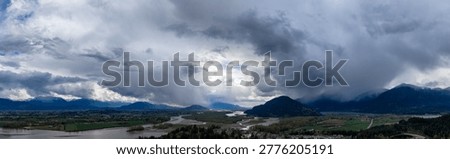Dramatic storm clouds rolling over the Fraser Valley river floodplain and mountains; Cloudscape in Fraser Valley, British Columbia, Canada.