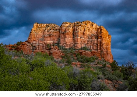 Dramatic storm clouds rolling over the vibrant red sandstone cliffs of Courthouse Butte during sunset in Sedona, Arizona.