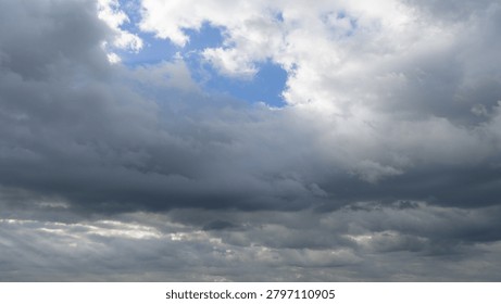 Dramatic Storm Clouds with Sun Rays Breaking Through Overcast Sky. A dramatic sky filled with dark gray storm clouds and textured overcast formations. Sunbeams break through gaps in the cloud cover, creating atmospheric rays of light and a moody weather scene. Natural cloudscape background with changing weather conditions, suitable for themes of nature, climate, hope, spirituality, forecast, and environmental concepts.