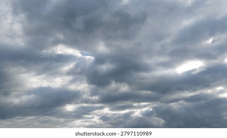 Dramatic Storm Clouds with Sun Rays Breaking Through Overcast Sky. A dramatic sky filled with dark gray storm clouds and textured overcast formations. Sunbeams break through gaps in the cloud cover, creating atmospheric rays of light and a moody weather scene. Natural cloudscape background with changing weather conditions, suitable for themes of nature, climate, hope, spirituality, forecast, and environmental concepts.