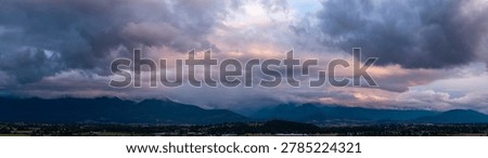 Dramatic storm clouds sweep across the Chilliwack mountain range at sunset, forming a moody British Columbia panorama.