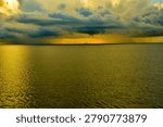 Dramatic storm front over golden ocean waters at sunset with distant fishing boat
