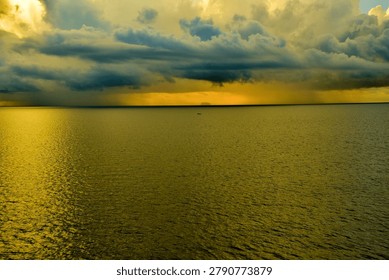 Dramatic storm front over golden ocean waters at sunset with distant fishing boat