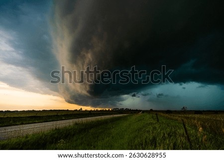 Dramatic storm sweeps across fields and farmland with heavy wind and rain, dark clouds moving fast, creating an ominous, moody sky filled with texture, shadow, and epic weather atmosphere