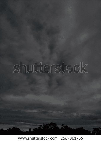 Dramatic, stormy clouds loom over the horizon, creating an ominous and moody atmosphere. Silhouettes of trees enhance the scene's mystery, as the dark clouds dominate the view with an intense presence