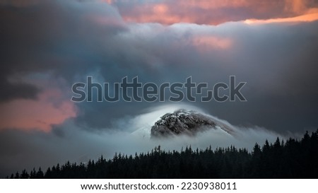 Dramatic Stormy Clouds over the Snowy Mountains of Hoverla snow covered peak in Ukraine. Dramatic light nature forest silhouette background. Hoverla is the higest Ukrainiam mountain. Famous symbol