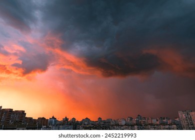 Dramatic stormy cloudy sky in red sunset tones over modern residential buildings of the city district.